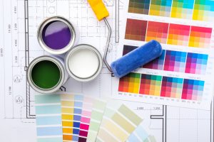Open paint cans in purple, white, and green with a paint roller rest on architectural blueprints. Various color swatches hint at a design or renovation project underway by a professional residential painting company in Nassau County, NY.