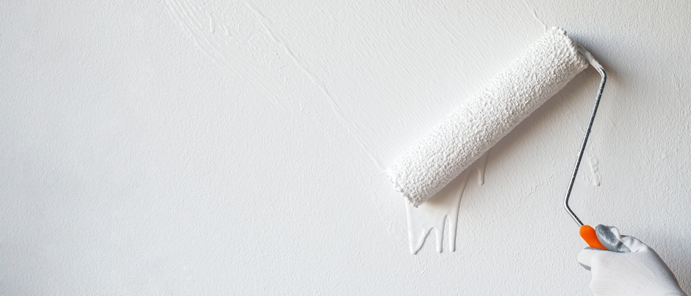 A gloved hand uses a paint roller to apply white paint on a smooth wall, expertly reflecting the precision expected from an Interior Painting Nassau County NY company.